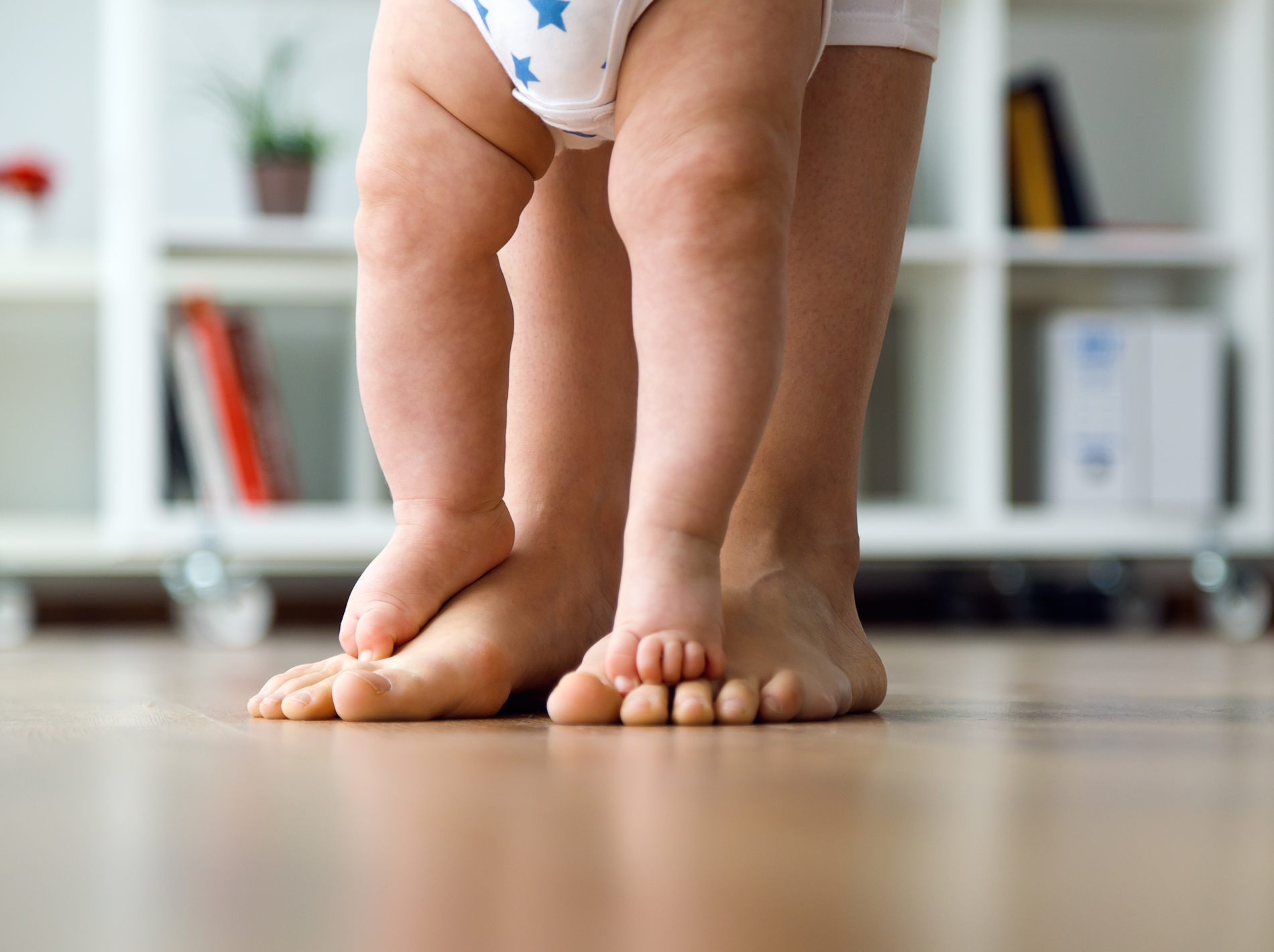 A baby walks on an adult's feet